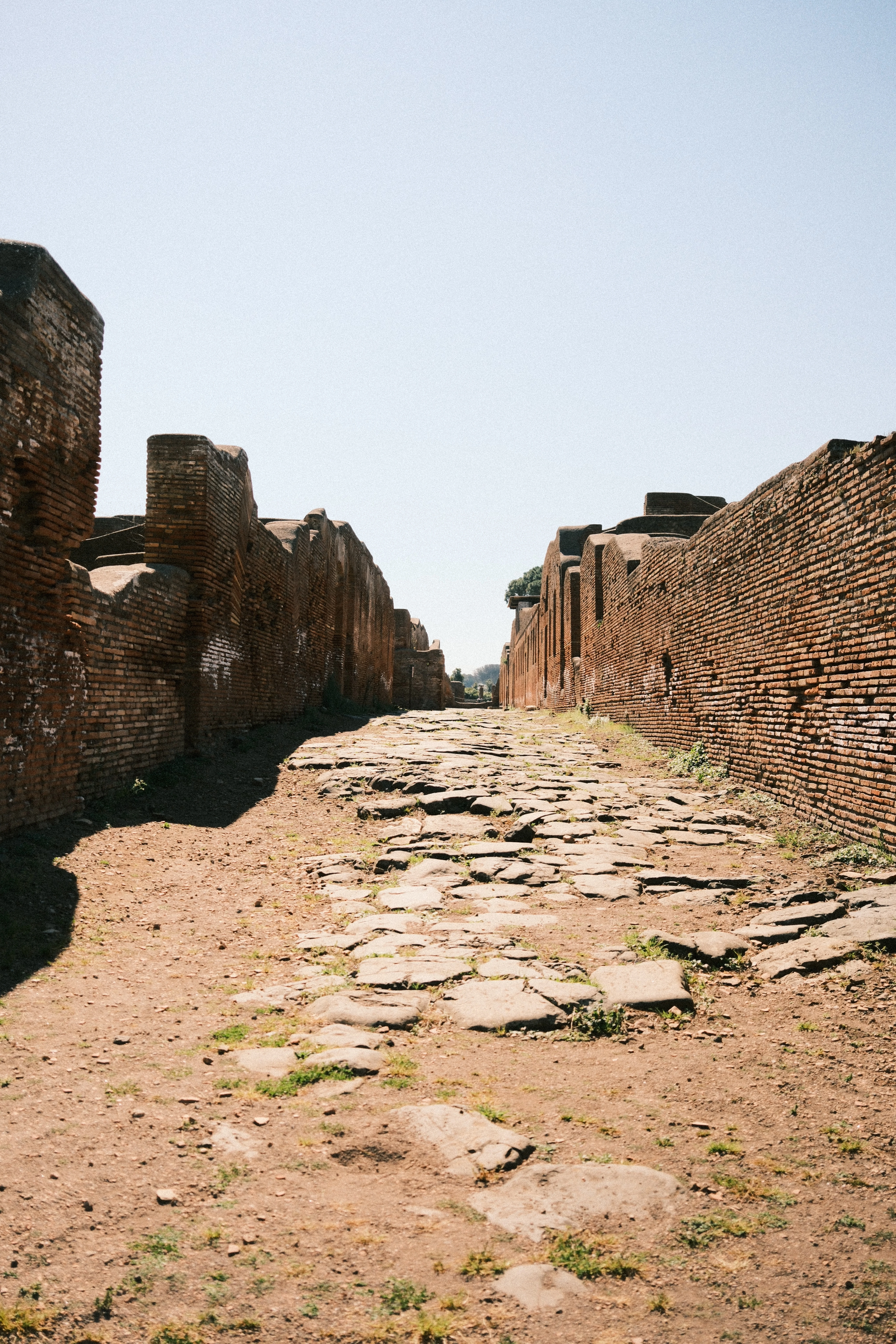 A stone-paved street running away between low brick walls in hard sunlight.