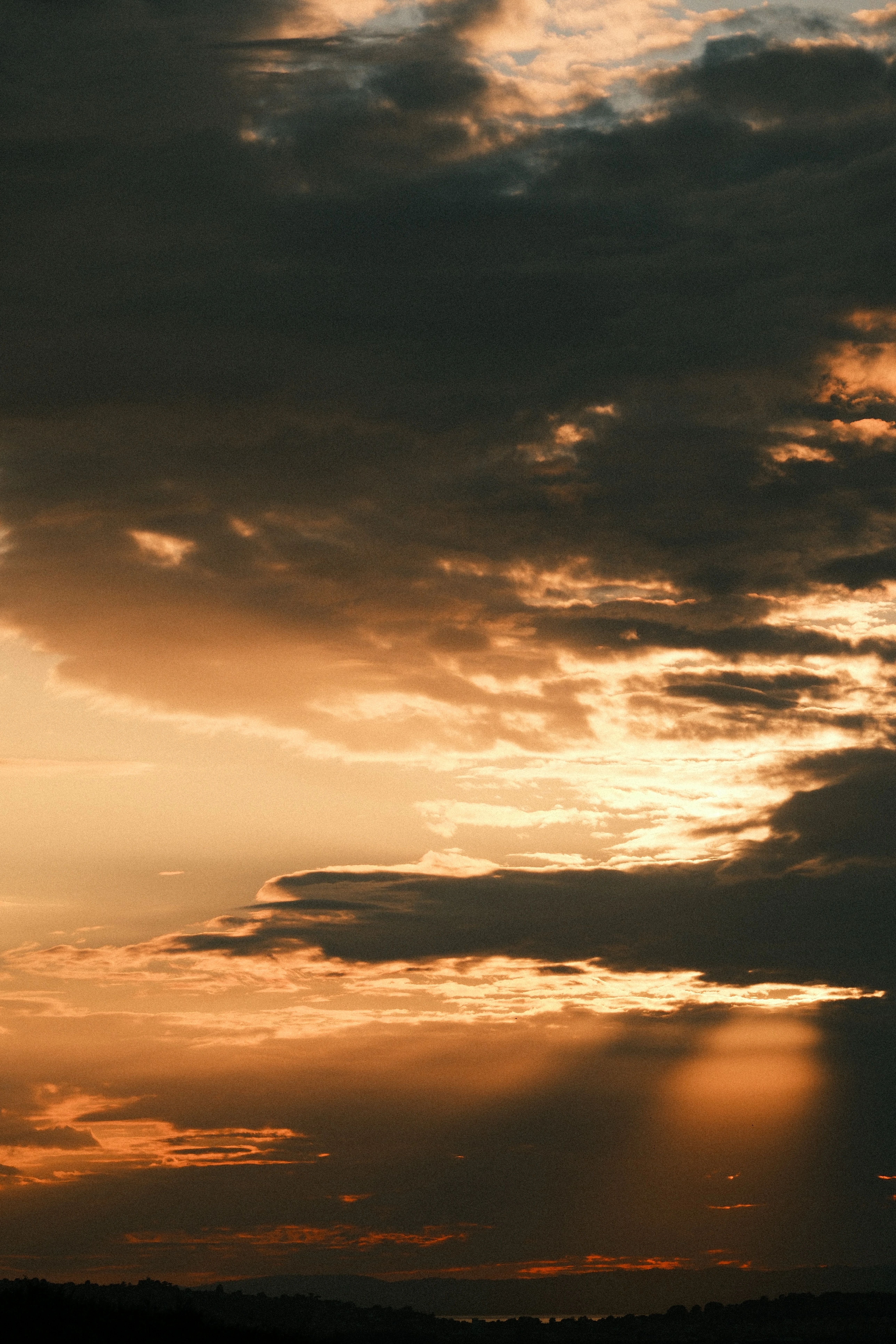 Heavy cloud at sunset with shafts of light falling toward a dark line of hills.