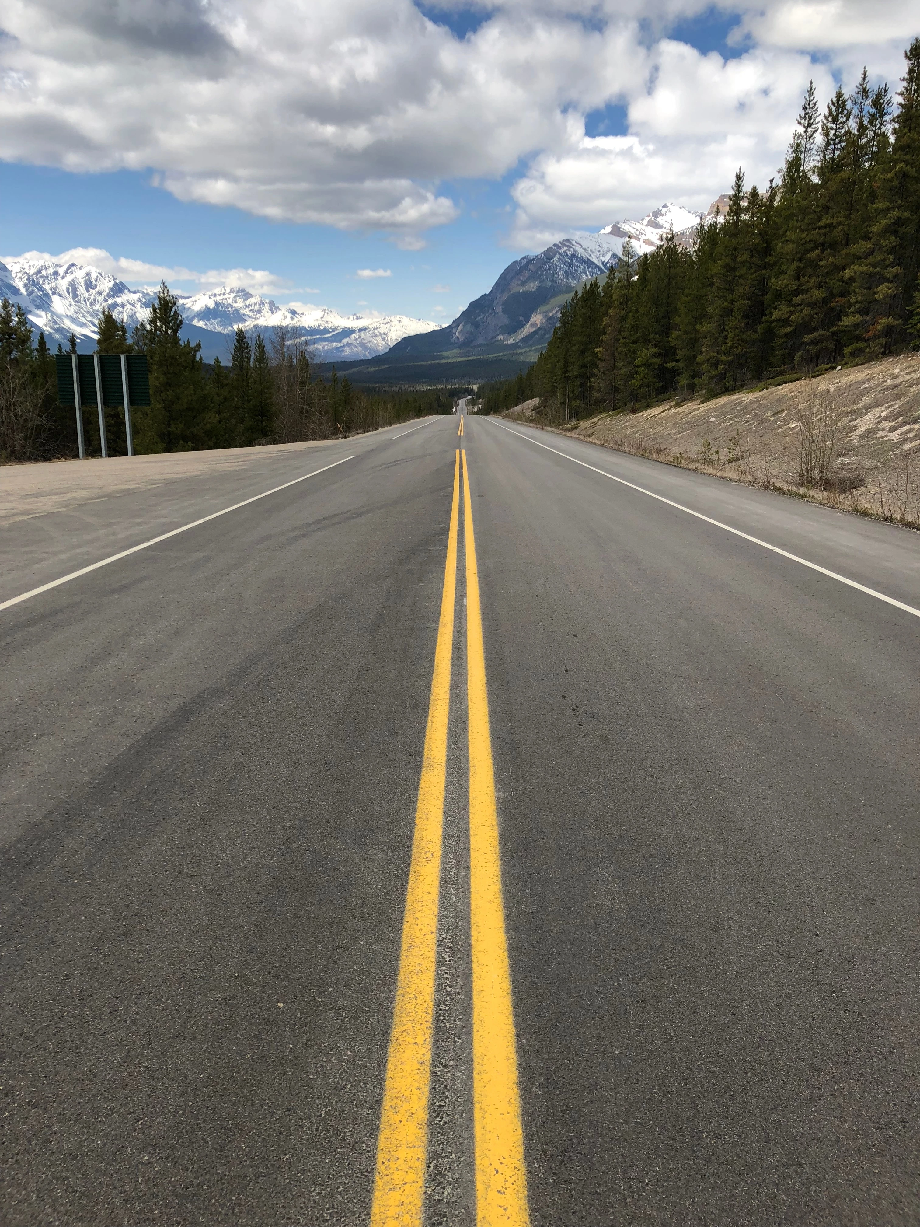 A road photographed from its centre line, running dead straight toward snow-covered mountains.