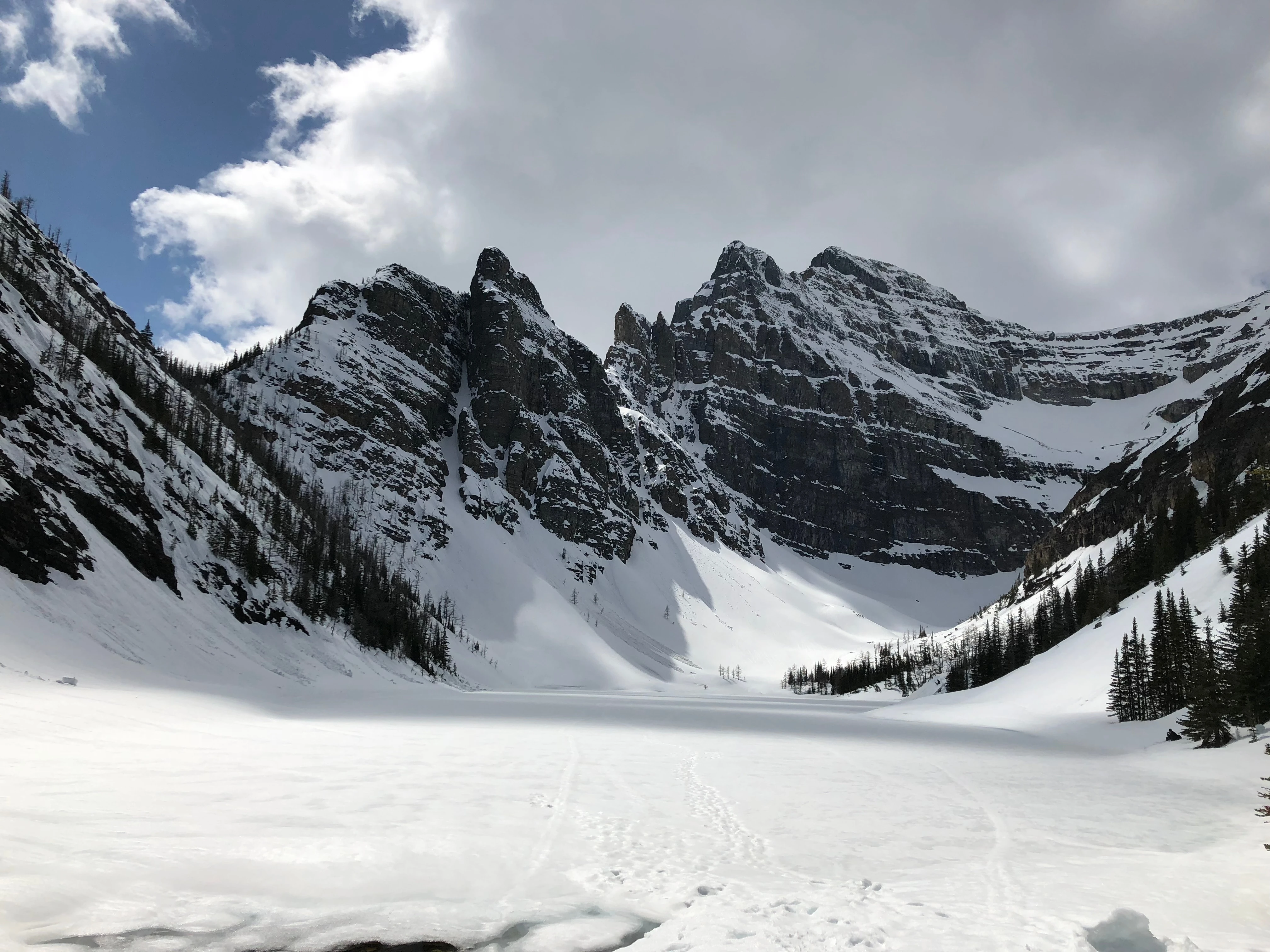 A frozen lake in a steep rock bowl, with tracks crossing the snow toward dark cliffs.