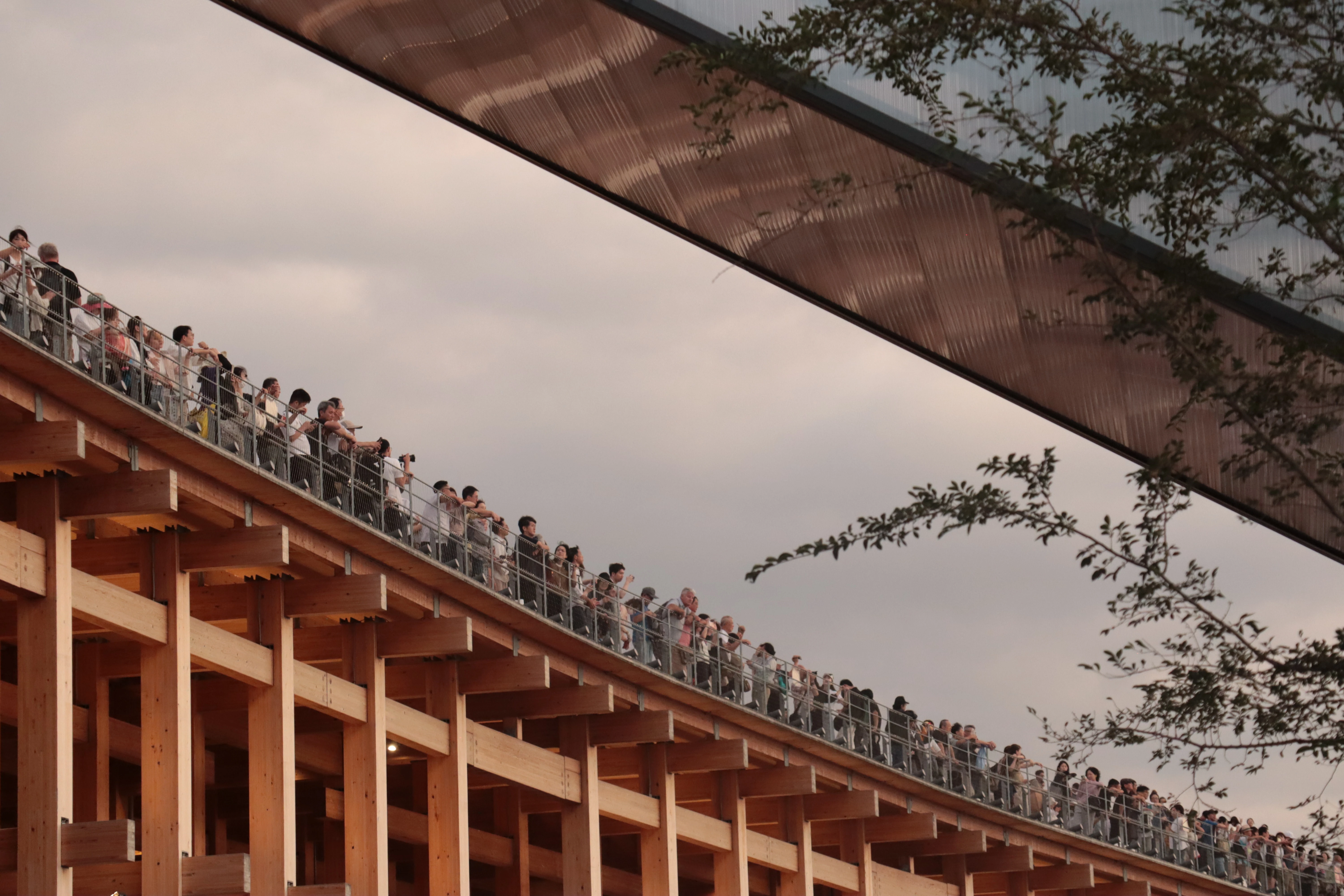 A long timber structure cutting diagonally across the frame, with a dense line of people along its upper walkway.