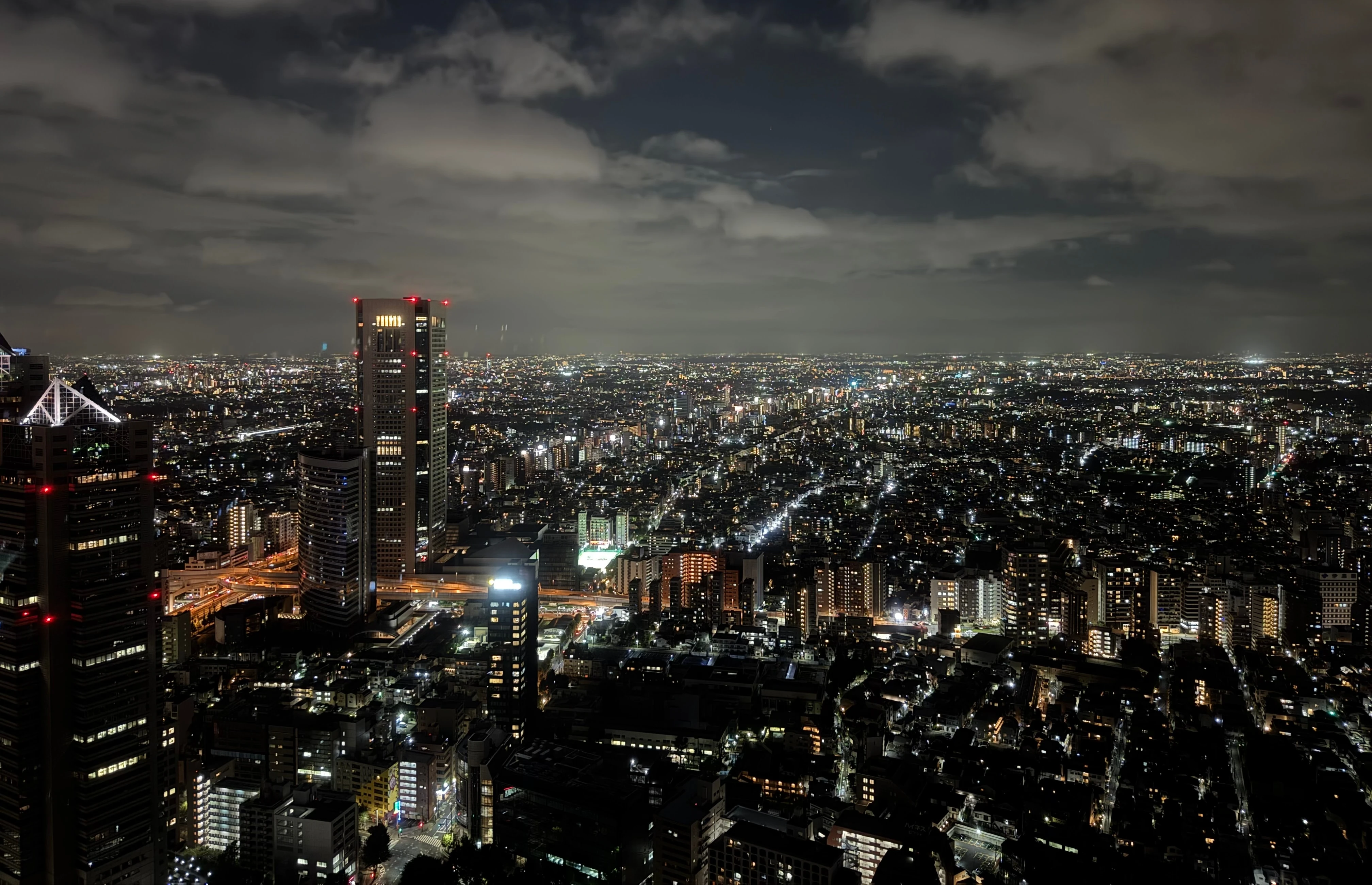 A city spread to the horizon at night, lit orange and white under a heavy cloud ceiling catching the light.