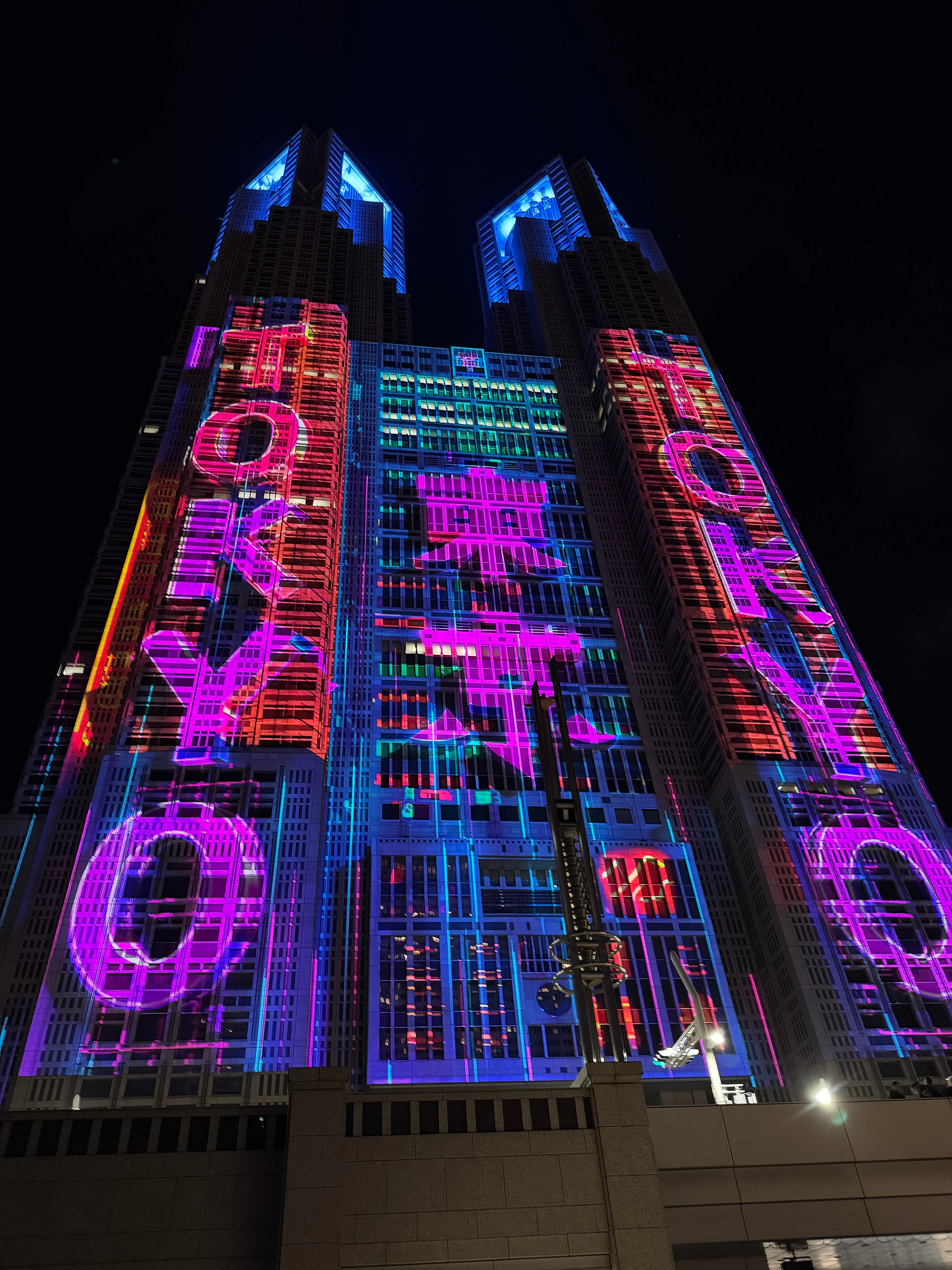 Twin tower blocks at night with vivid pink, purple and blue projections thrown across their facades.